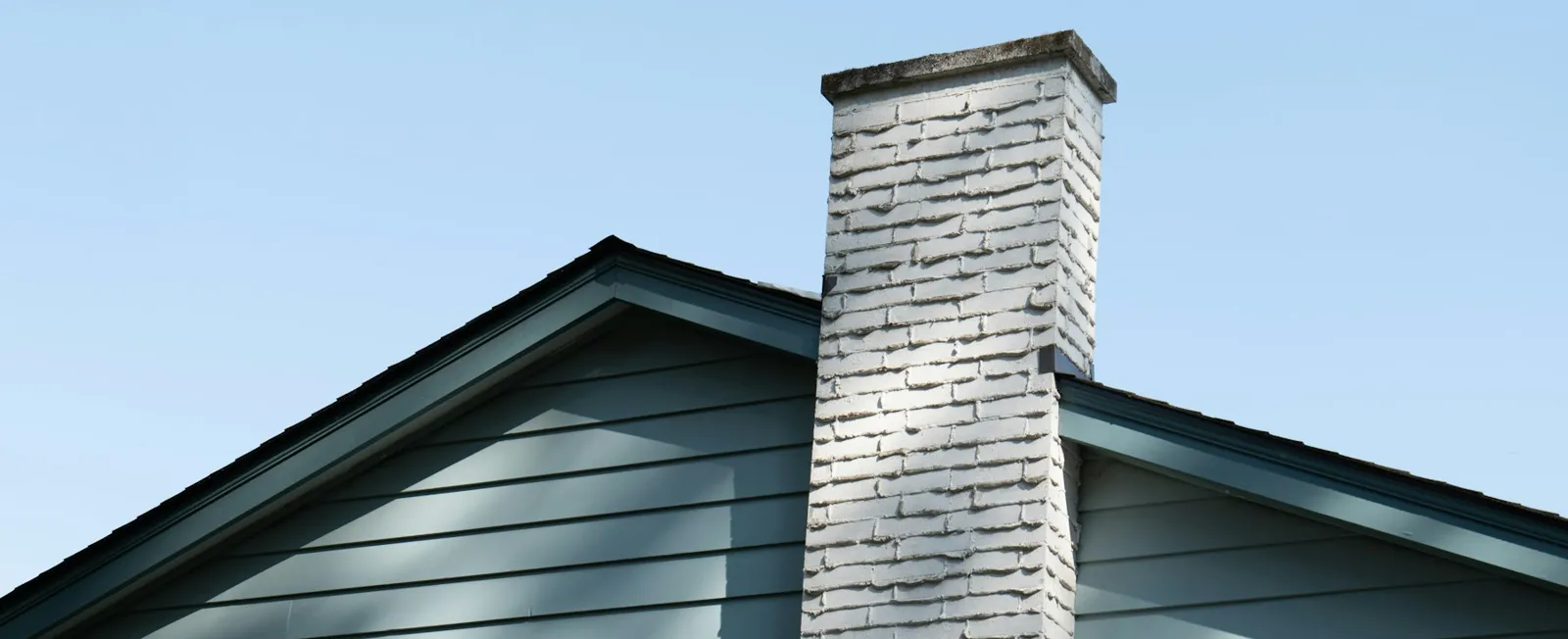 Painted white brick chimney rising above a blue-sided house roofline