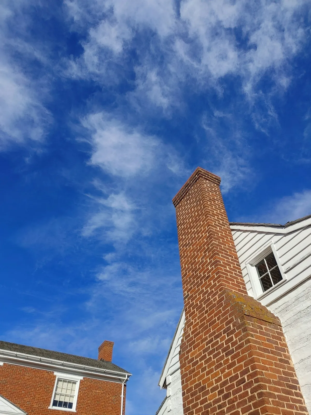 Tall red brick chimney beside white siding under a blue sky