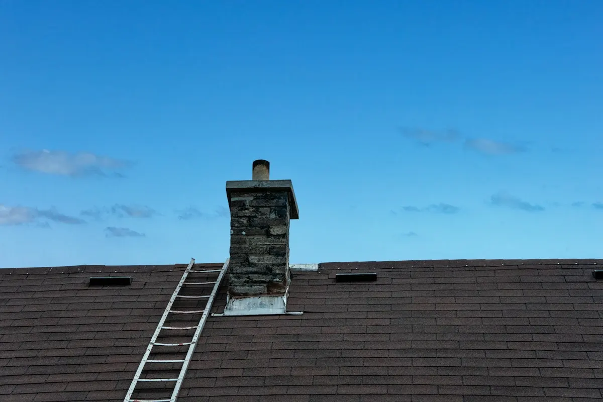 Brick chimney on a shingle roof with a ladder